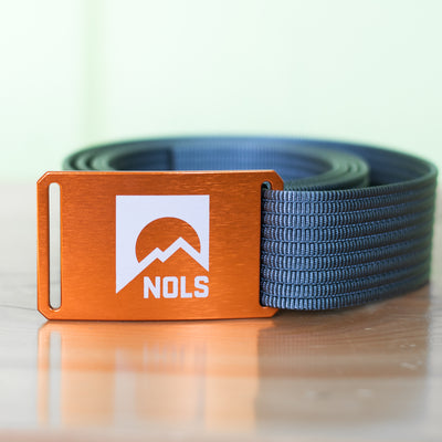 GRIP6 Belt with NOLS Logo featuring an orange aluminum buckle with white mountain logo design on navy blue nylon webbing, showcasing a minimalist and durable adjustable belt design